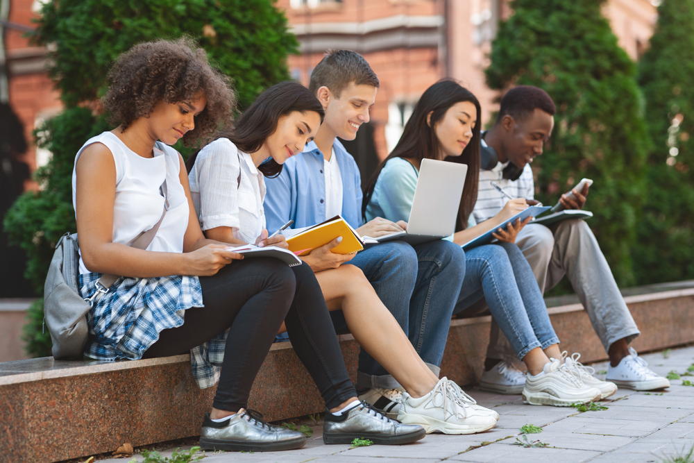 Focused students preparing for exams outdoors in the university courtyard, sitting on bench in campus